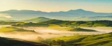 İtalya, San Quirico d 'Orcia' da gündoğumunda Val d 'Orcia vadisinin sisli sabah güneşli tepeleri arasında selvi ağaçlarıyla çevrili bir ev.
