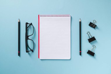 Mavi ofis masasında boş defter, gözlük ve kalem üst görünümü