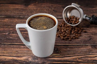 Amerikan kahvesini beyaz porselen bardakta, ahşap masada dinlendiriyorum.