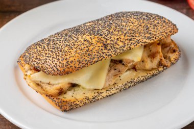 Çedar peyniri ve tavuklu sandviç. Tahta masadaki beyaz porselen tabakta.