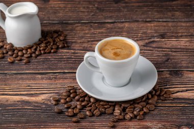 Beyaz porselen bardakta espresso macchiato. Süt ve kahve çekirdekleri ahşap masada.