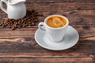 Beyaz porselen bardakta espresso macchiato. Süt ve kahve çekirdekleri ahşap masada.
