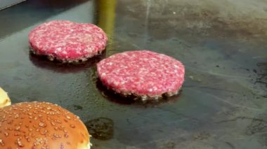 Düz bir ızgarada kızarmış hamburger köfteleri ve yanında hamburger çörekleri.