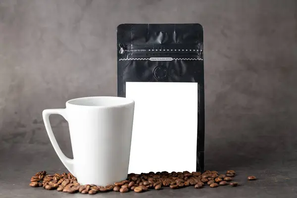 Black coffee foil packaging bag and coffee cup with blank white label on stone table