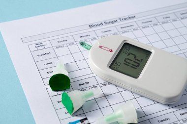 Mavi arka planda glukometre, tükenmez kalem, şeritler ve kan şekeri takip cihazının üst görüntüsü. Diyabet test kiti