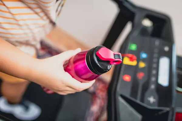 stock image Young girl running on the treadmill with a sports water bottle in hand