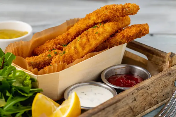 Fish and chips with fresh greens and sauces on wooden table