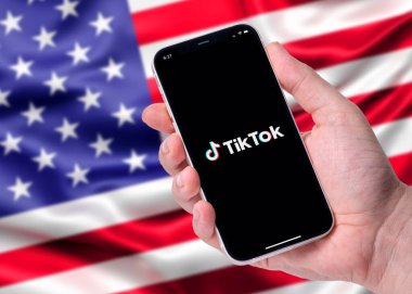 Antalya, Türkiye - 15 Mart 2024: Bulanık Amerikan bayrağının önünde duran akıllı telefonun ekranında TikTok logosu