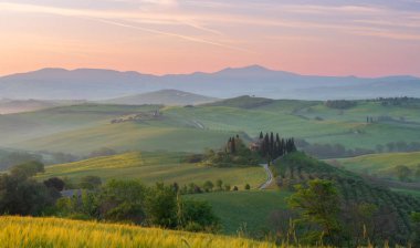 Pienza, Toskana, İtalya - 13 Nisan 2024 San Quirico d 'Orcia, İtalya' daki Val d 'Orcia vadisinin sisli sabah güneşli tepeleri arasında selvi ağaçlarıyla çevrili ev