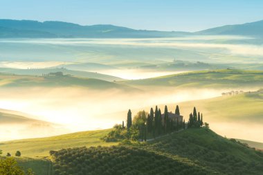 Pienza, Toskana, İtalya 13 Nisan 2024, San Quirico d 'Orcia, Tuscany, İtalya' da gün doğumunda güneşle sırılsıklam olmuş Val d 'Orcia vadisinin sisli tepeleri arasında selvi ağaçlarıyla çevrili ev.