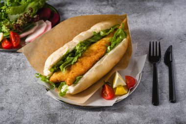 Taş masada yeşil sebzeli kızarmış balık sandviçi. Türkçe adı Balik Ekmek