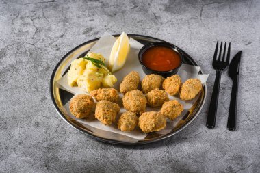 Metal bir tabakta kızarmış midye ve yanında patates salatası. Türkçe adı: Midye Tava