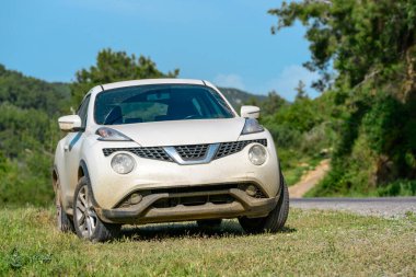 Çamurla kaplı mini SUV yol kenarında yeşillikte oturuyor.