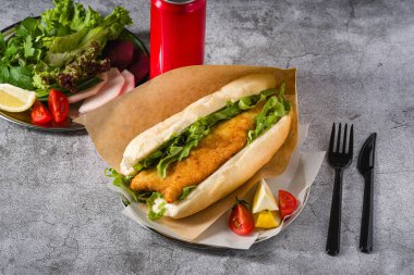 Taş masada yeşil sebzeli kızarmış balık sandviçi. Türkçe adı Balik Ekmek