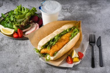 Taş masada yeşil sebzeli kızarmış balık sandviçi. Türkçe adı Balik Ekmek