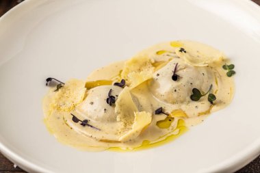 Beyaz porselen tabakta soslu peynirli ravioli.