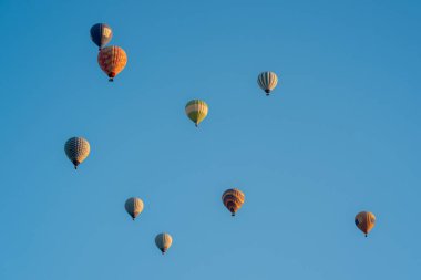 Koyu mavi, kırmızı ve sarı renkli sıcak hava balonları hafif bulutlu mavi gökyüzünde uçuyor.