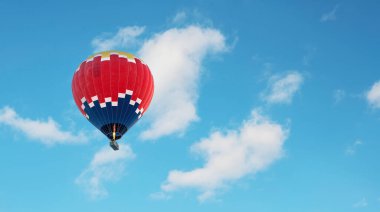 Koyu mavi, kırmızı ve sarı renkli sıcak hava balonu hafif bulutlu mavi gökyüzünde uçuyor.