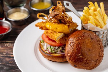 Kızarmış patates ve sosla servis edilen tavuk burgeri beyaz porselen tabakta.