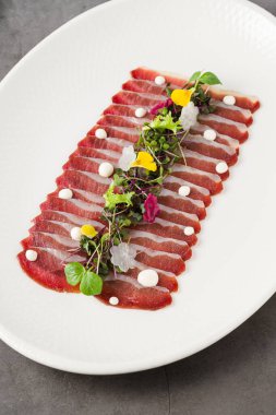 Beyaz porselen tabakta taş masada füme ördek pastırması.