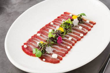 Beyaz porselen tabakta taş masada füme ördek pastırması.