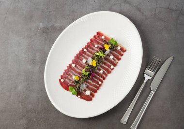 Beyaz porselen tabakta taş masada füme ördek pastırması.