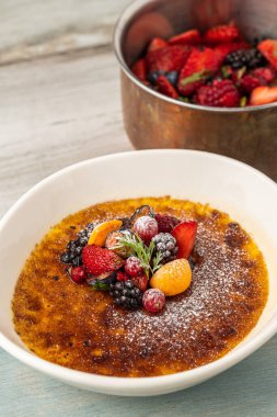 Meyve ve pudra şekerle süslenmiş, ahşap bir masada krem karamel.