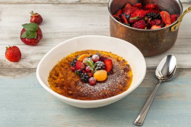 Meyve ve pudra şekerle süslenmiş, ahşap bir masada krem karamel.