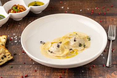 Beyaz porselen tabakta soslu peynirli ravioli.