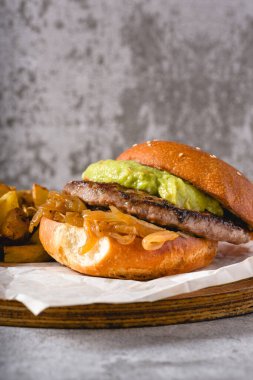 Tahta kesme tahtasında karamelli soğan ve avokado ile hamburger.