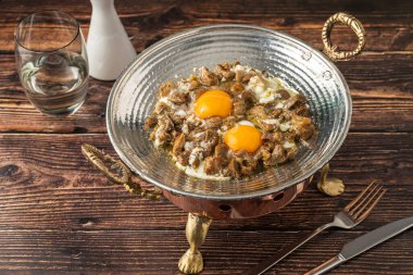 Ahşap bir masada bakır bir tavada kızartılmış etli yumurta. Türkçe adı kavurmali yumurta