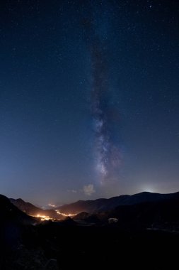 Bir vadideki bir kasabanın ışıklarının üzerindeki Samanyolu.