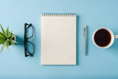 Mavi arkaplanda defter, bardak, kahve ve tükenmez kalem üst görünümü
