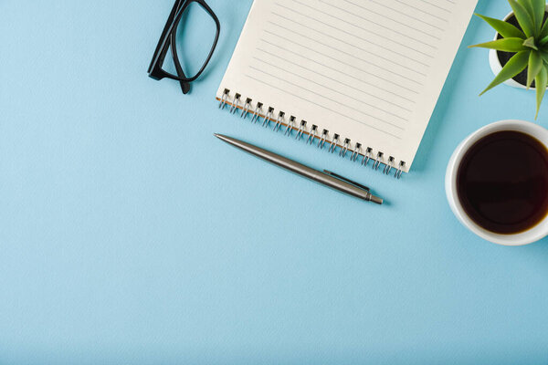 Top view of notebook, glasses, coffee and ballpoint pen on blue background