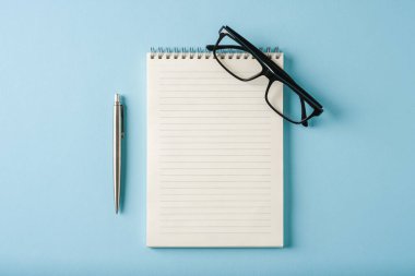 Mavi arkaplanda dizüstü bilgisayar, gözlük ve tükenmez kalem görünümü