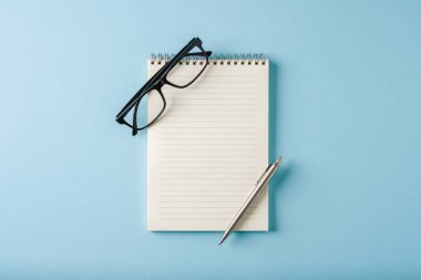 Mavi arkaplanda dizüstü bilgisayar, gözlük ve tükenmez kalem görünümü