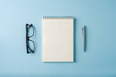 Mavi arkaplanda dizüstü bilgisayar, gözlük ve tükenmez kalem görünümü