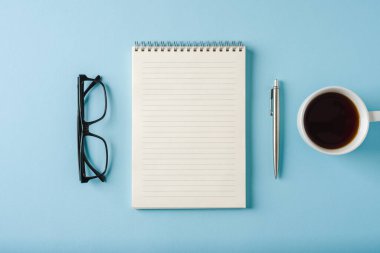 Mavi arkaplanda defter, bardak, kahve ve tükenmez kalem üst görünümü