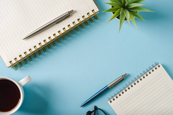 Top view of notebook, glasses, coffee and ballpoint pen on blue background