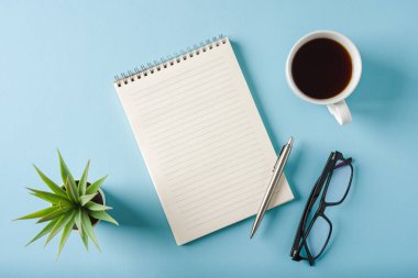 Mavi arkaplanda defter, bardak, kahve ve tükenmez kalem üst görünümü
