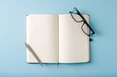 Mavi arkaplanda dizüstü bilgisayar, gözlük ve tükenmez kalem görünümü