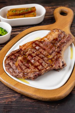 Grilled veal chop on white porcelain plate on wooden table