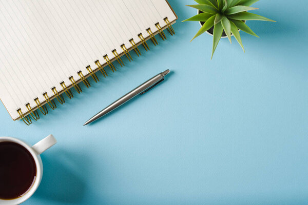 Top view of notebook, glasses, coffee and ballpoint pen on blue background