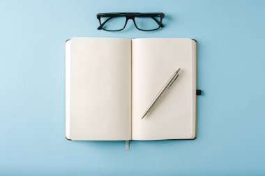 Mavi arkaplanda dizüstü bilgisayar, gözlük ve tükenmez kalem görünümü