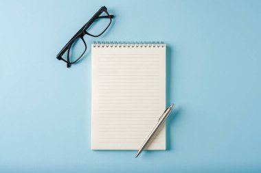 Mavi arkaplanda dizüstü bilgisayar, gözlük ve tükenmez kalem görünümü