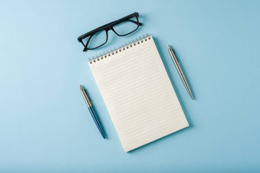 Mavi arkaplanda dizüstü bilgisayar, gözlük ve tükenmez kalem görünümü