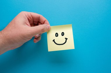 Elinde sarı yapışkan kağıt ya da mavi arkaplanda gülen ikon olan post-it.