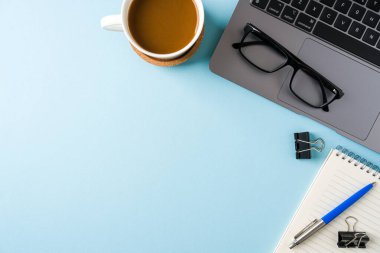 Kahve fincanı, dizüstü bilgisayar klavyesi ve mavi ofis masasında çeşitli kırtasiye malzemeleri. İş ofisi kavramı