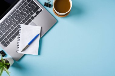 Kahve fincanı, dizüstü bilgisayar klavyesi ve mavi ofis masasında çeşitli kırtasiye malzemeleri. İş ofisi kavramı