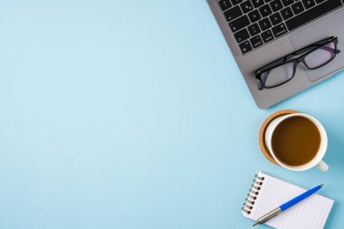 Kahve fincanı, dizüstü bilgisayar klavyesi ve mavi ofis masasında çeşitli kırtasiye malzemeleri. İş ofisi kavramı
